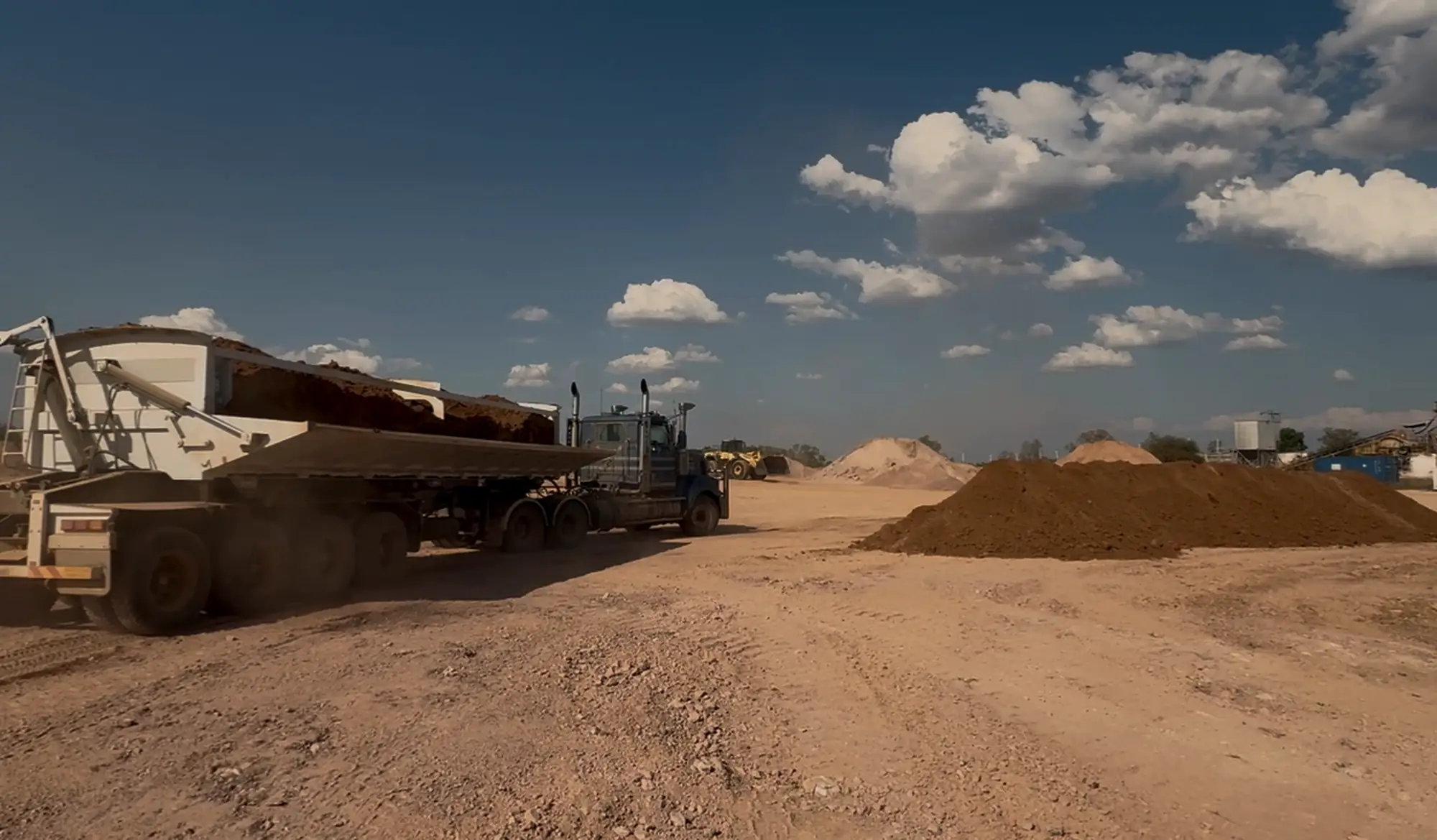 Road train with a loaded side-tipper trailer beside ore stockpiles